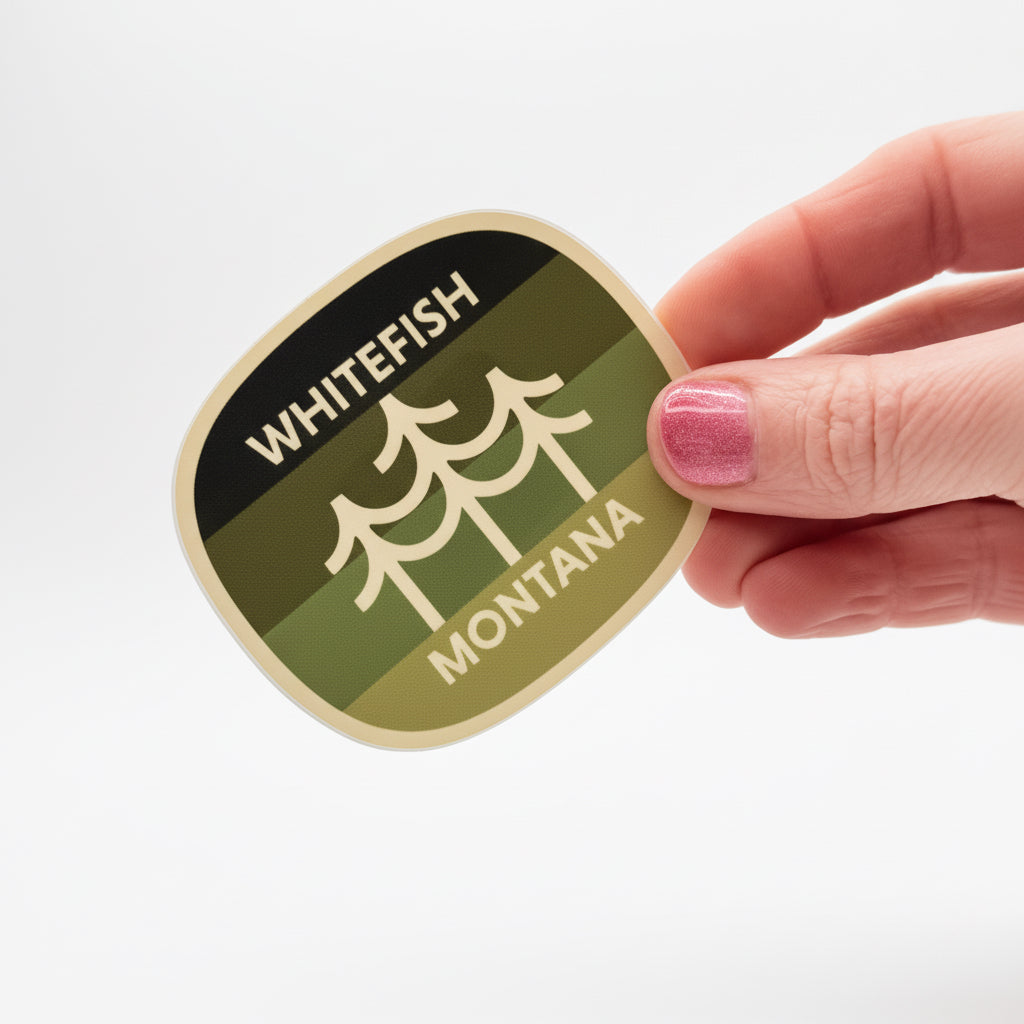 Hand holding a 'Whitefish Montana' sticker with a green and brown design.
