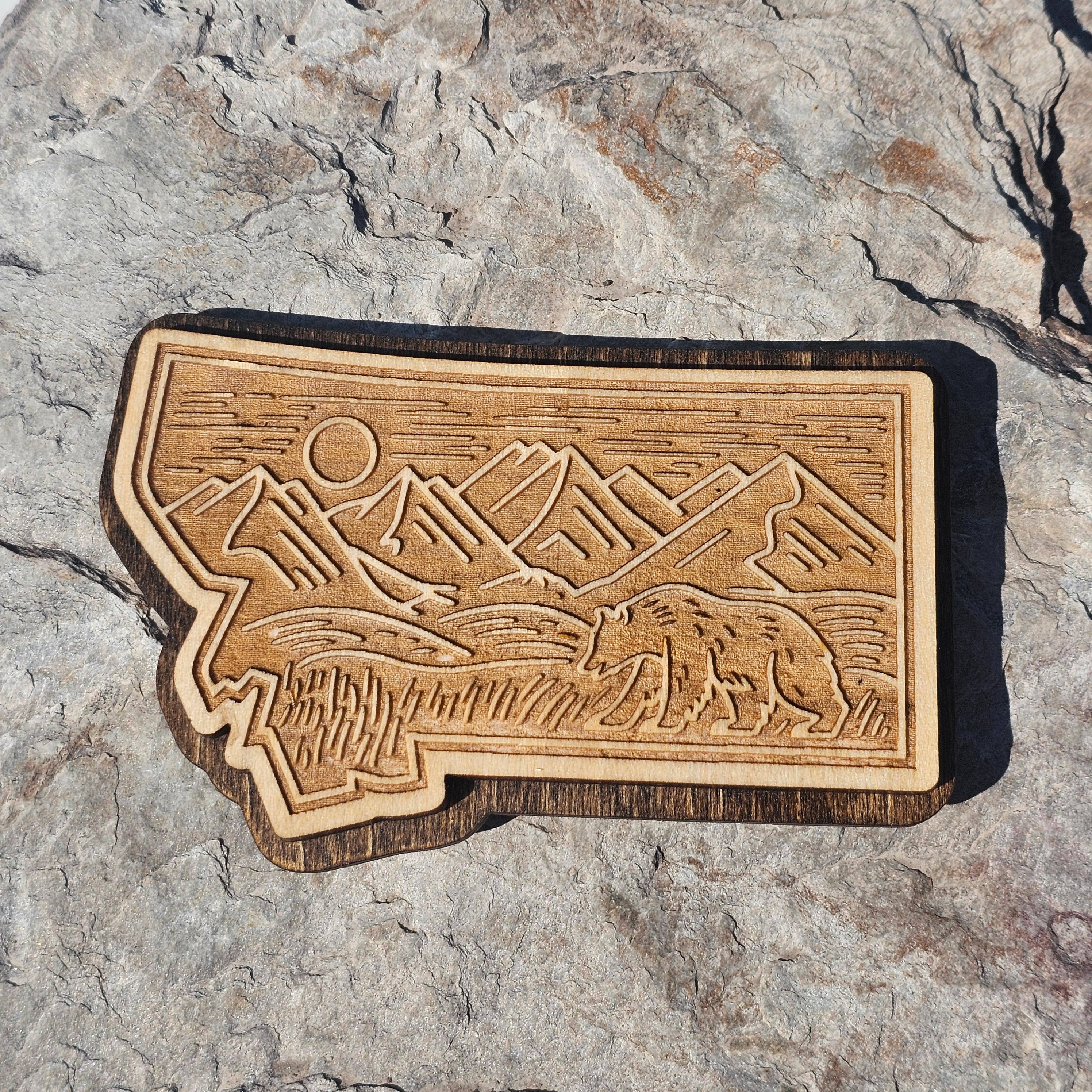 Engraved wood Montana state magnet with a mountain range, sun, and grazing grizzly bear, from The Ruddy Duck in Whitefish, Montana