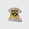 Sticker with a raccoon illustration and text 'Even Baddies Get Saddies' on a beige background