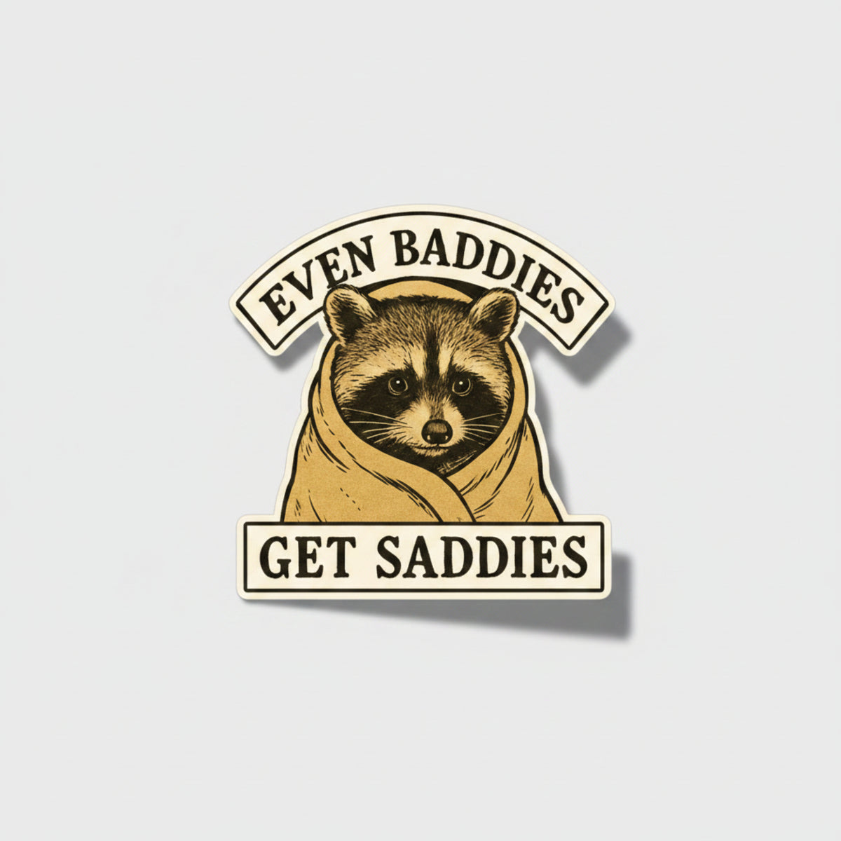 Sticker with a raccoon illustration and text 'Even Baddies Get Saddies' on a beige background