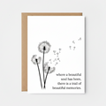 Greeting card with dandelion illustration and quote on a white surface with candles.