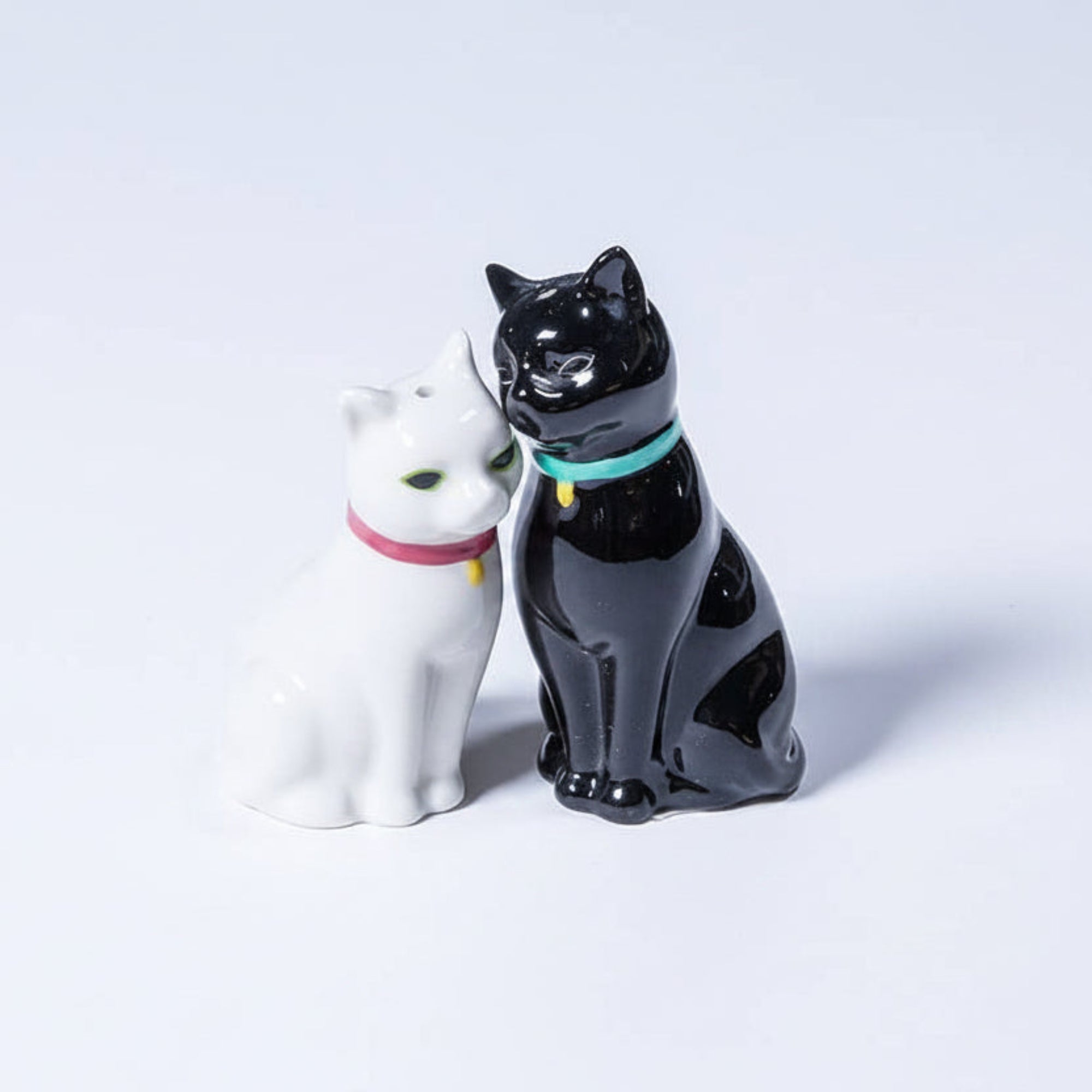 Two ceramic cat figurines, one white and one black, on a white surface.