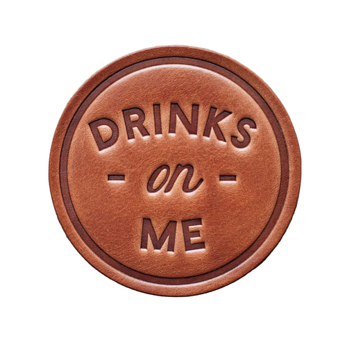 Brown leather sign with 'DRINKS on ME' text on a wooden background