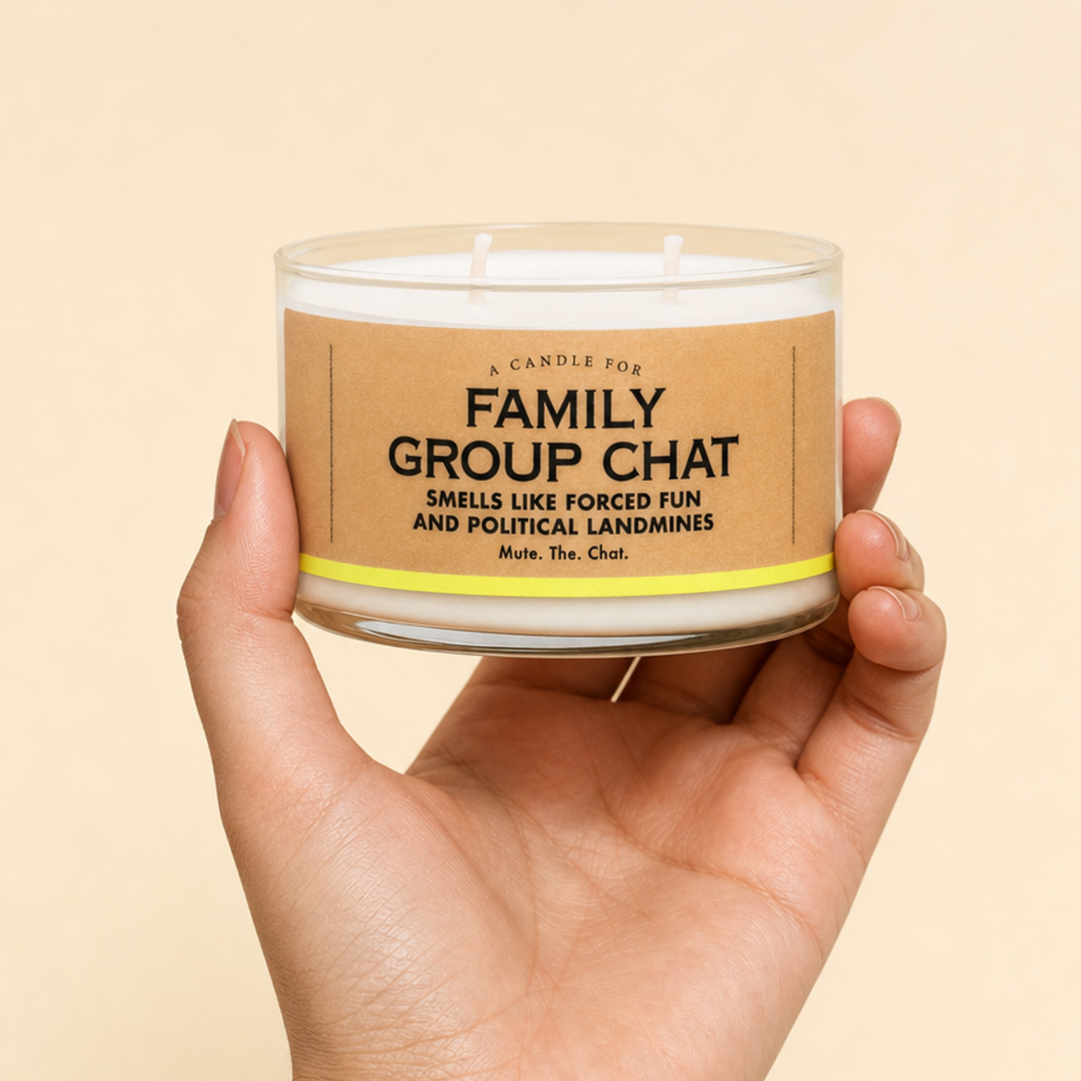 A hand holding a clear glass jar candle with a kraft paper label that reads 'FAMILY GROUP CHAT' on a warm beige background.
