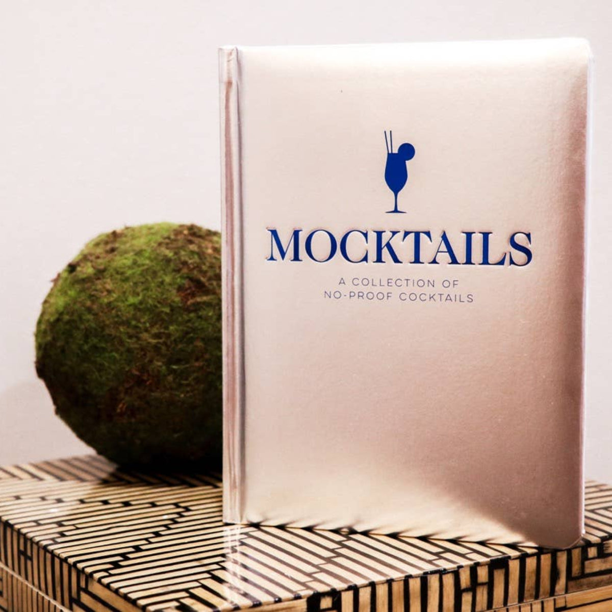 Book titled 'Mocktails' on a woven mat with a plant and decorative items.