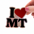 Hand holding a glittery 'I ❤️ MT' magnet on a white background