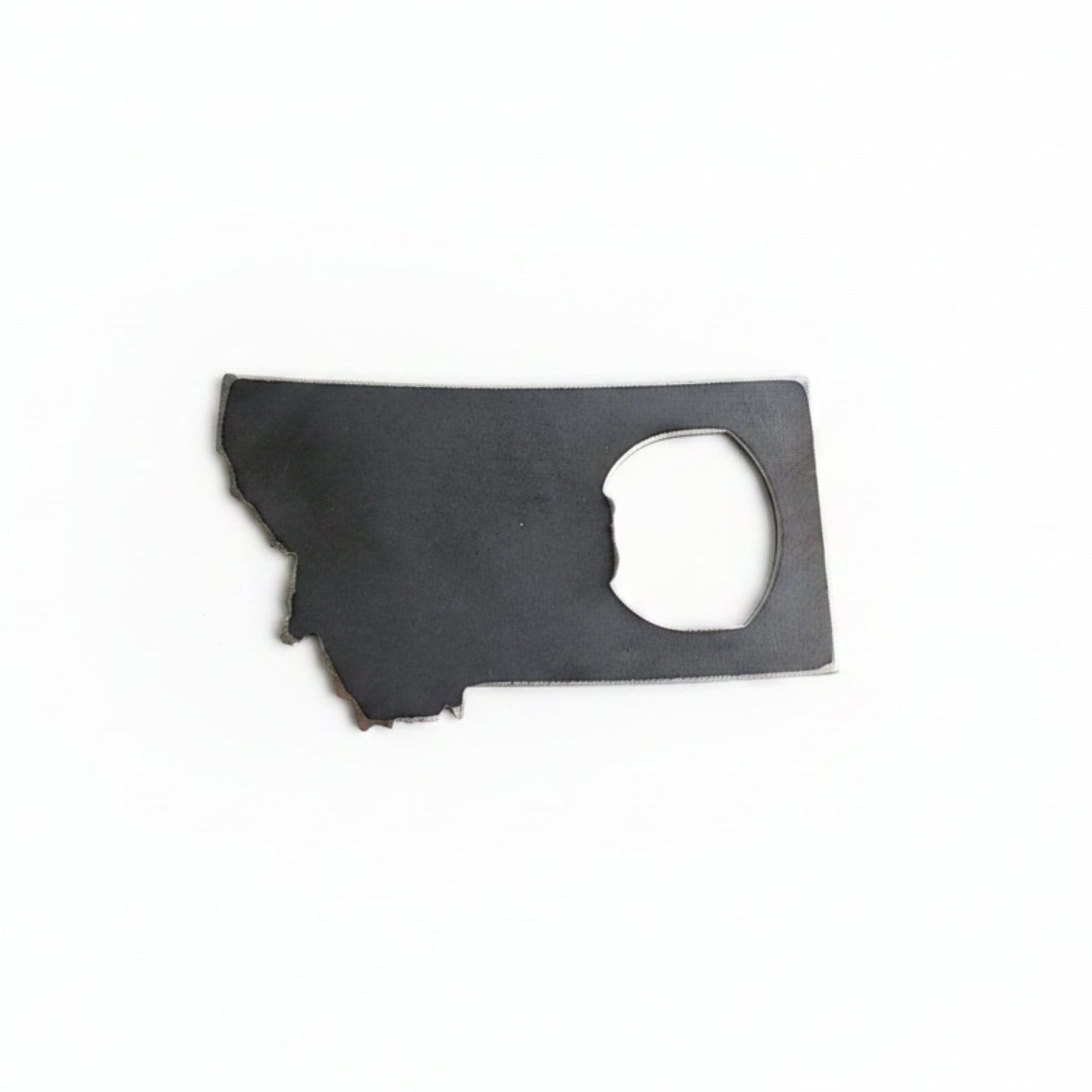 Metal bottle opener shaped like the state of Montana on a white wooden surface 