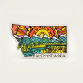 Colorful sticker shaped like the state of Montana with a landscape design on a white background.