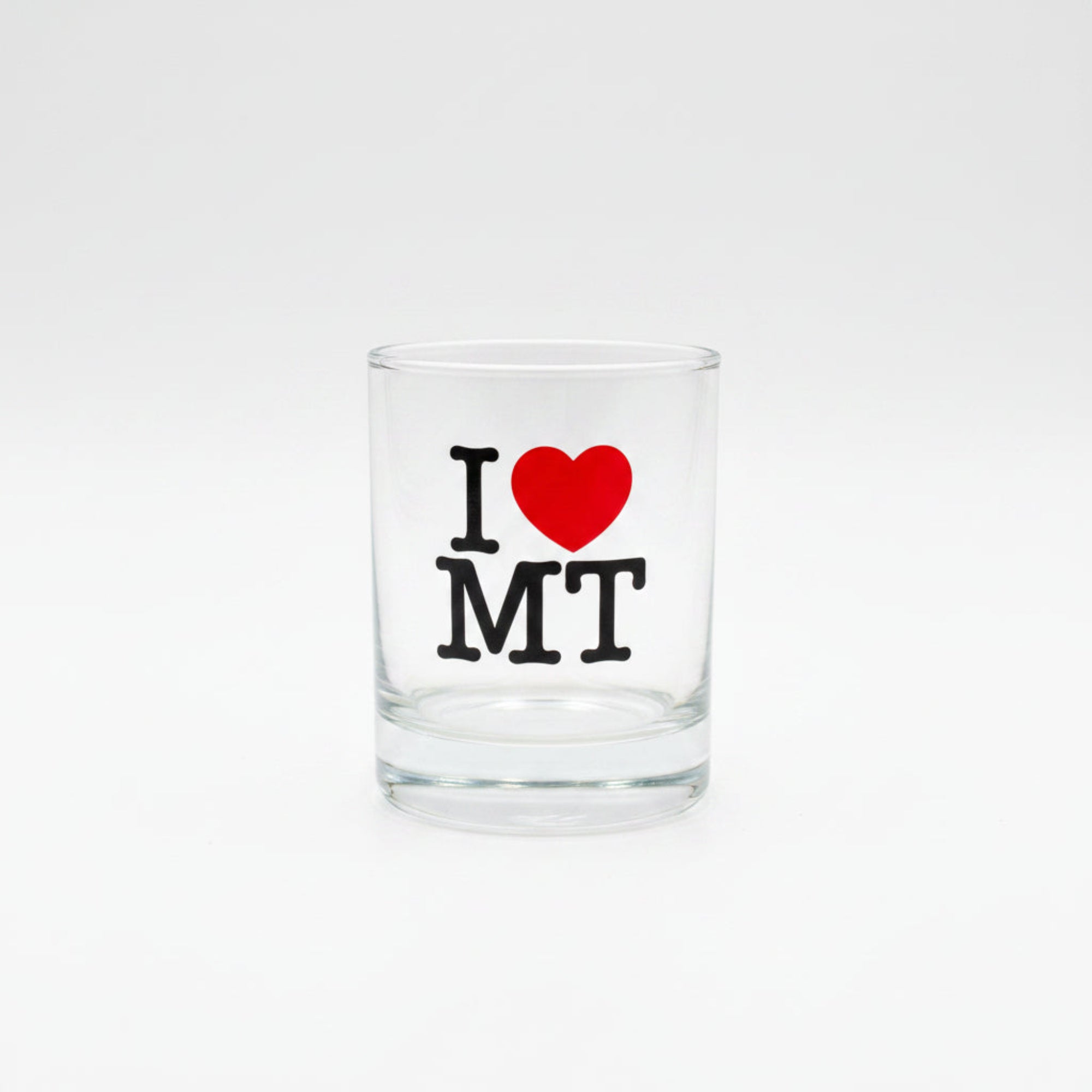 Clear glass shot glass with 'I ❤️ MT' text on a wooden surface