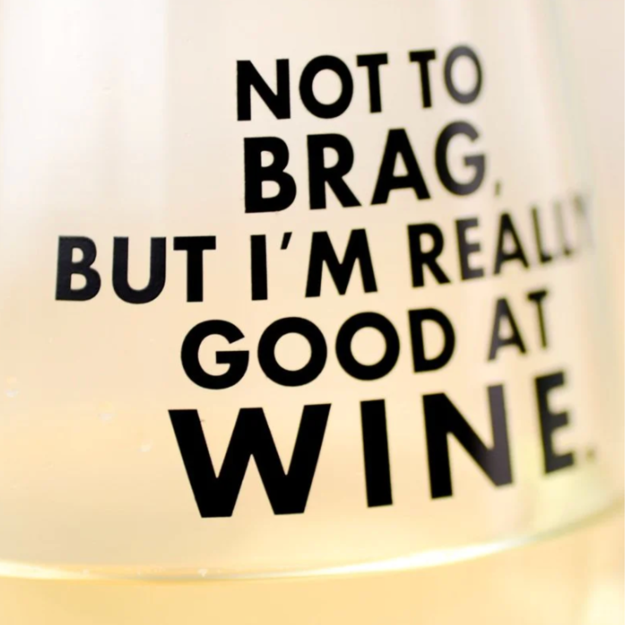 Glass with text 'Not to brag, but I'm really good at wine' on a white background