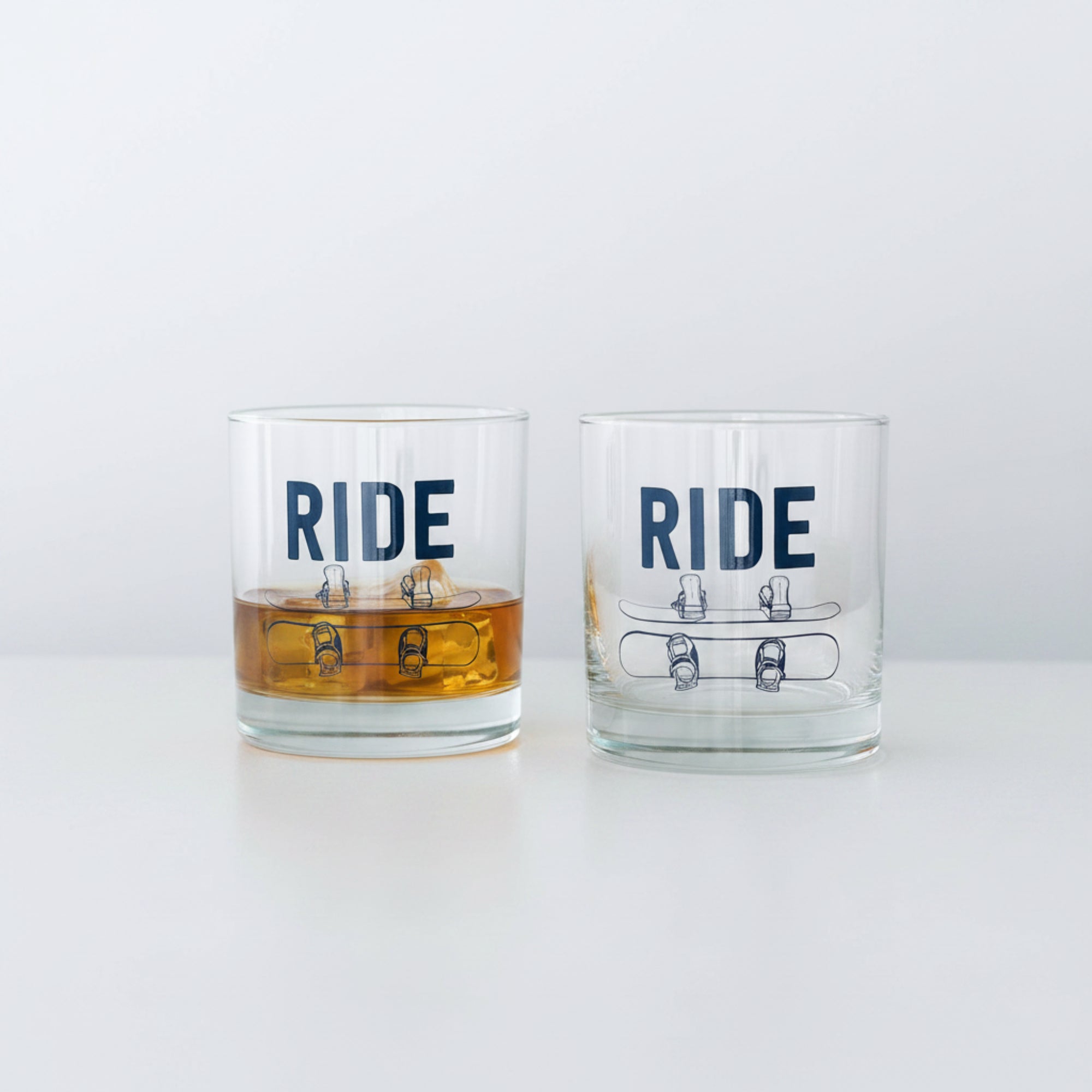 Two glass tumblers with 'RIDE' text on a wooden surface against a light gray background