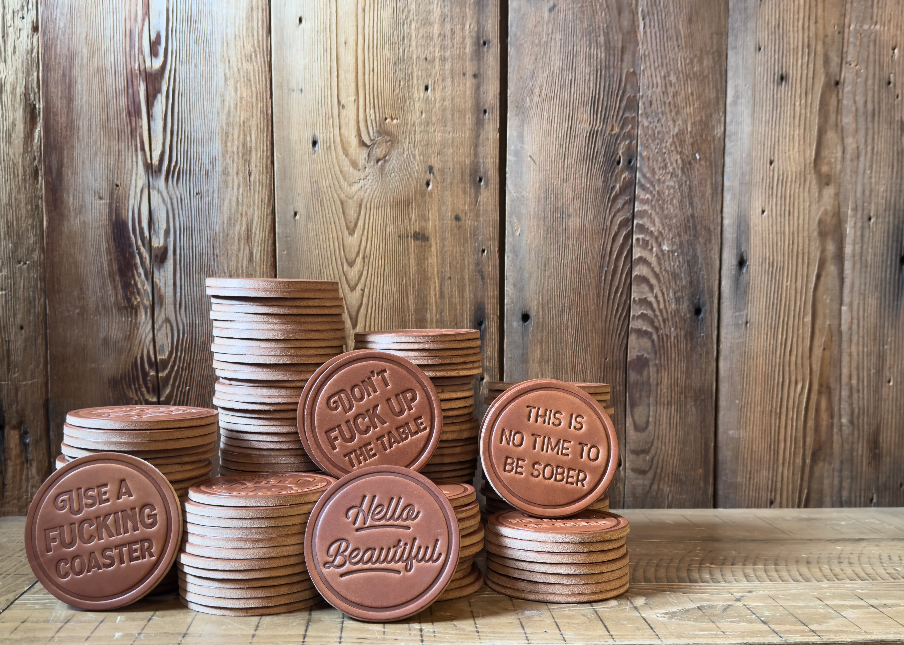Stacks of brown leather coasters with embossed text on a wooden surface and background