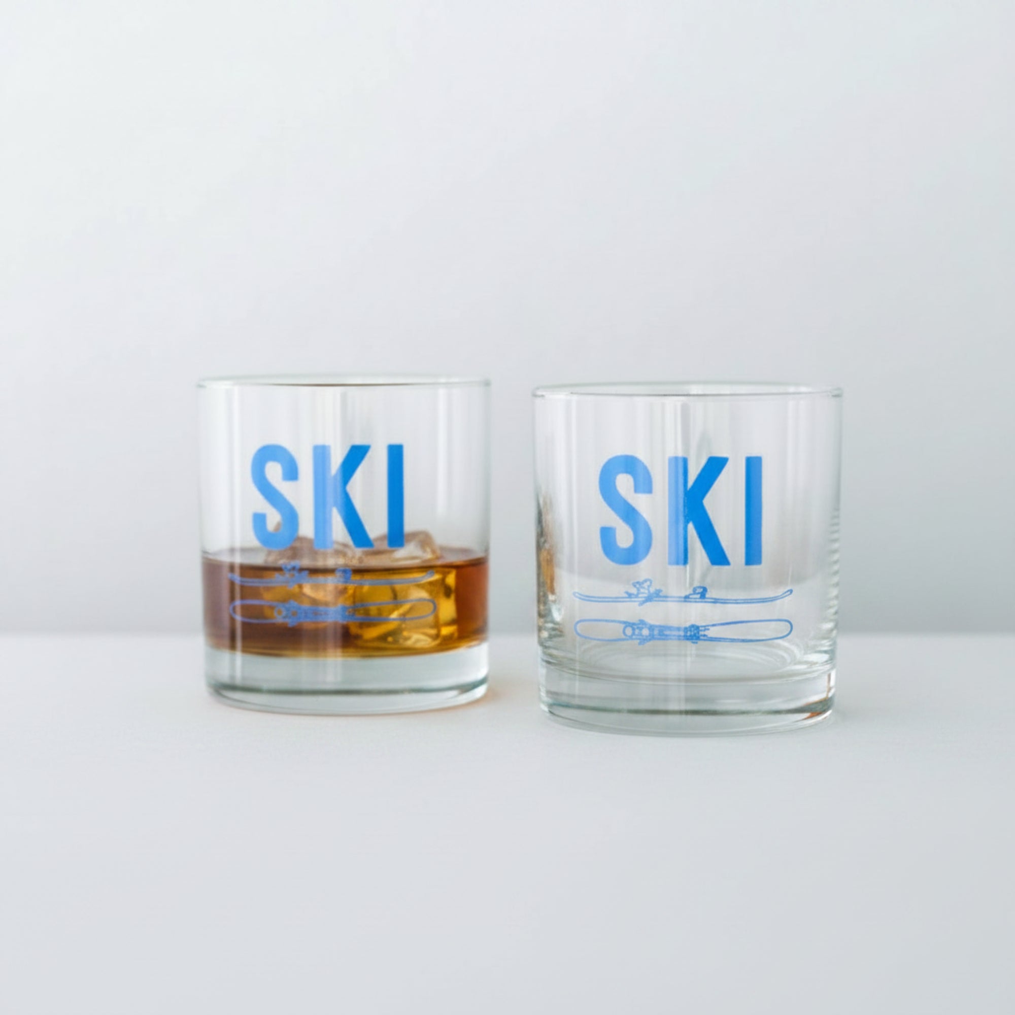 Two glasses with 'SKI' text on a wooden surface against a white background