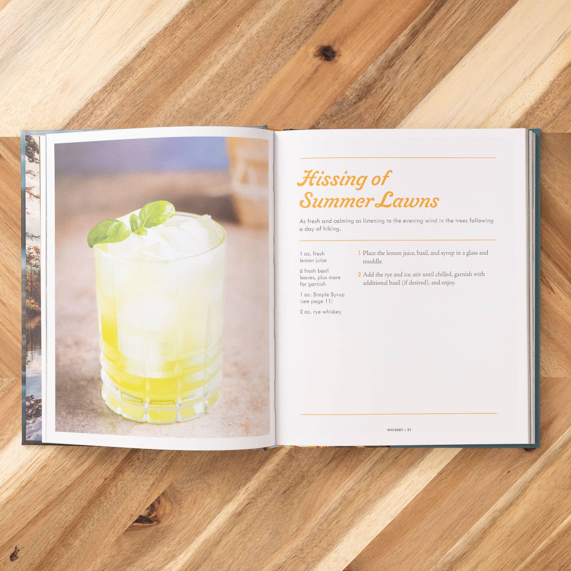 Open book on a wooden surface with a cocktail image and text.