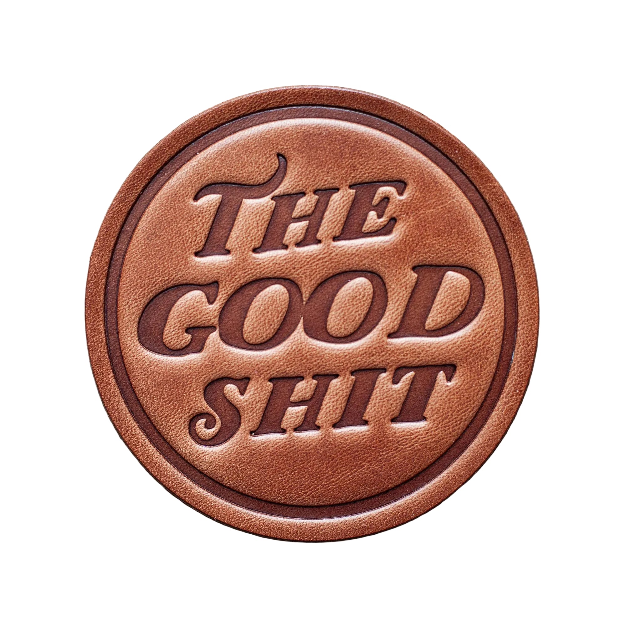 Round brown leather patch with 'The Good Shit' text on a wooden background