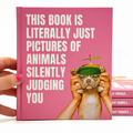 Book titled 'This Book is Literally Just Pictures of Animals Silently Judging you' with a pink cover and humorous text, held by a hand.