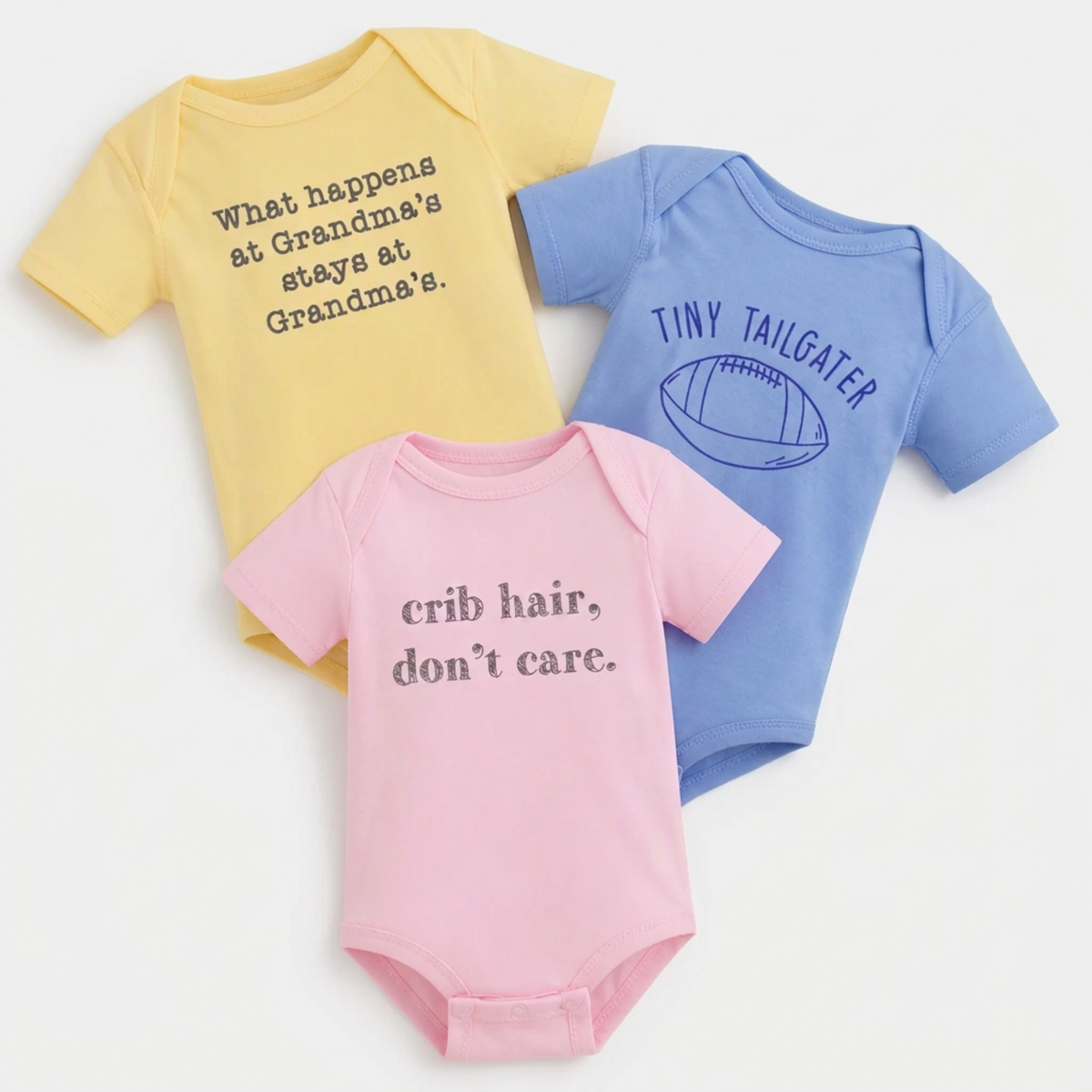 Three pastel baby onesies with funny sayings styled with baby shoes and wooden toys