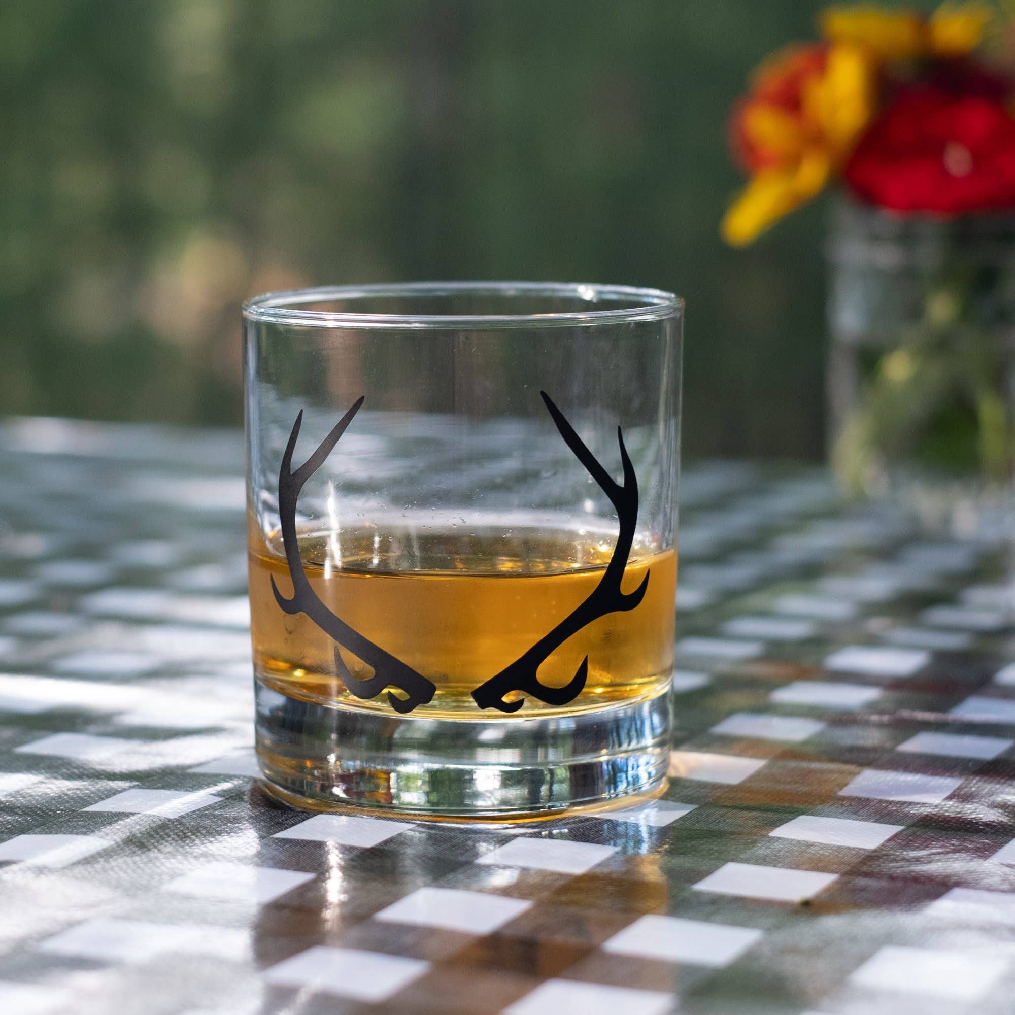 Glass with antler design filled with a yellow liquid on a checkered tablecloth.