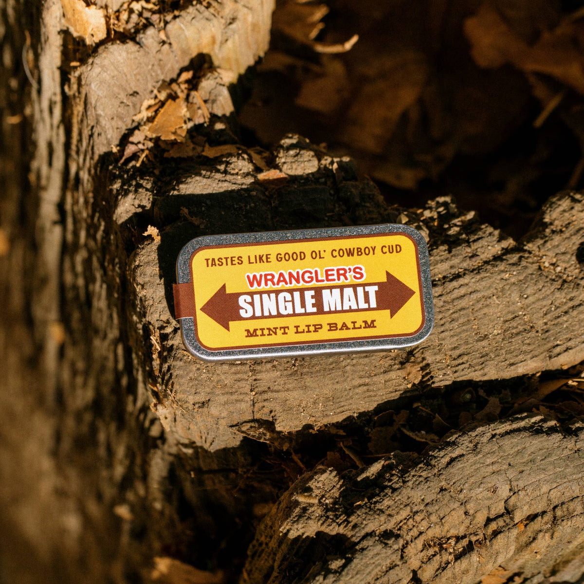 Lip balm labeled 'Wrangler's Single Malt Mint Lip Balm' on a wooden surface