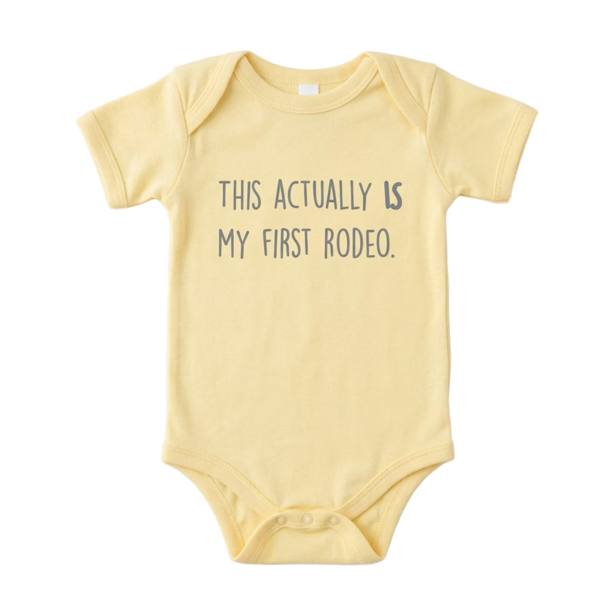 Yellow baby onesie that says This Actually IS My First Rodeo in gray lettering, from The Ruddy Duck in Whitefish, Montana