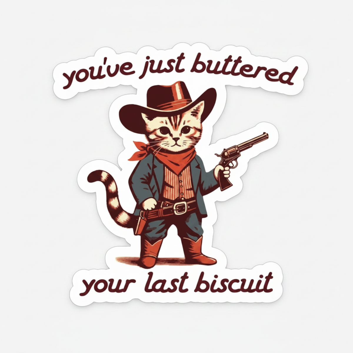 A die-cut sticker featuring a cartoon cat dressed as a cowboy with the text 'you've just buttered your last biscuit', shown on a dark wood background.
