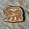 Layered wood bear magnet with an engraved forest and river scene inside the walking bear silhouette, from The Ruddy Duck in Whitefish, Montana