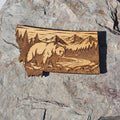 Deep engraved wood Montana state magnet showing a grizzly bear beside a winding river with mountains and pines, from The Ruddy Duck in Whitefish, Montana