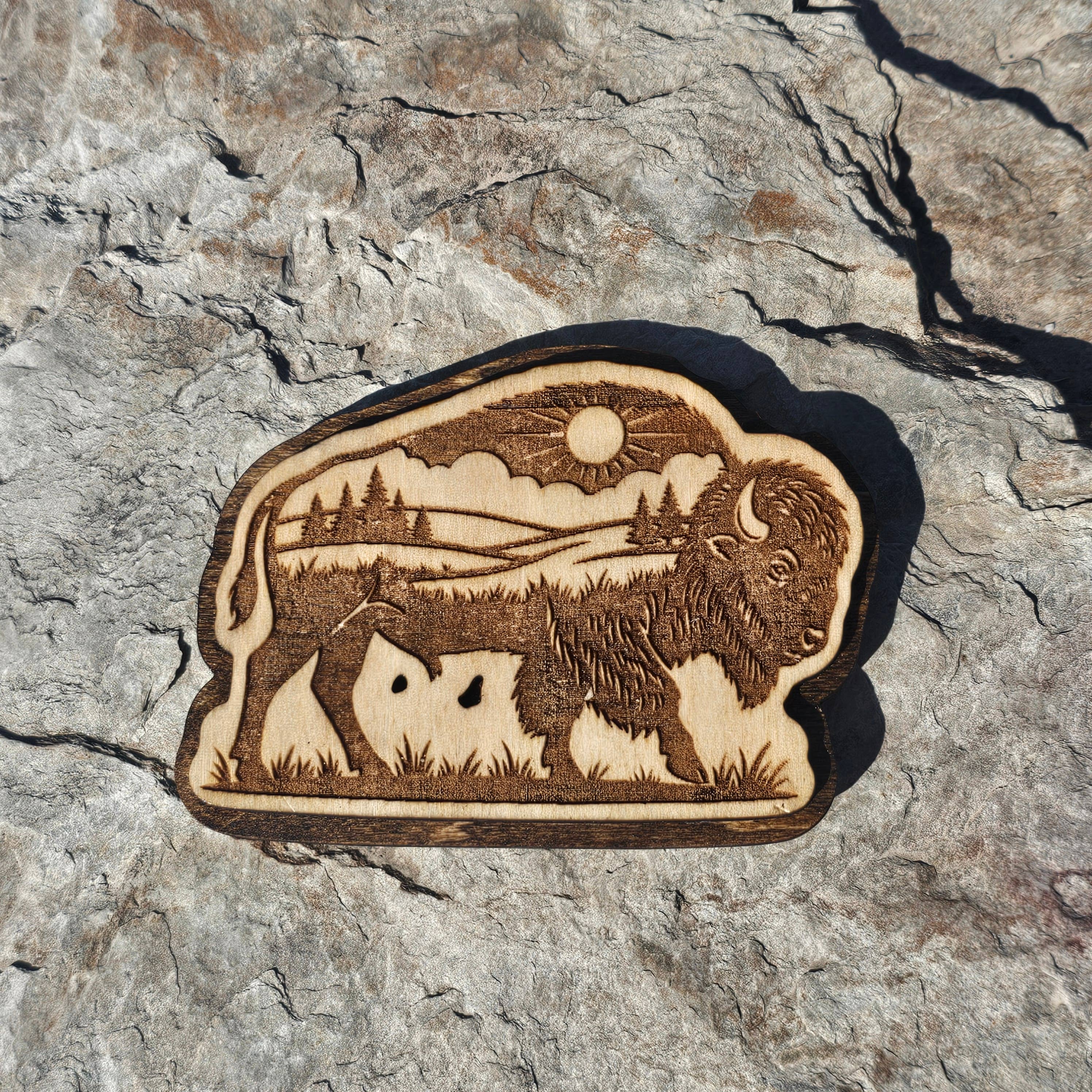 Layered wood bison magnet with an engraved prairie scene of sun, clouds, and pines, from The Ruddy Duck in Whitefish, Montana